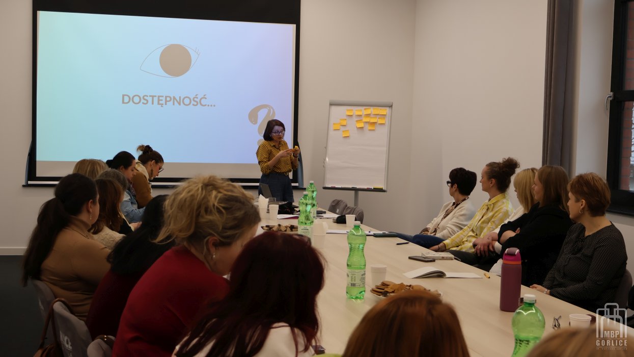 Biblioteka Gorlice, Szkolenie o odstępności bibliotekarze siedzą przy stole, a prowadząca omawia ćwiczenie